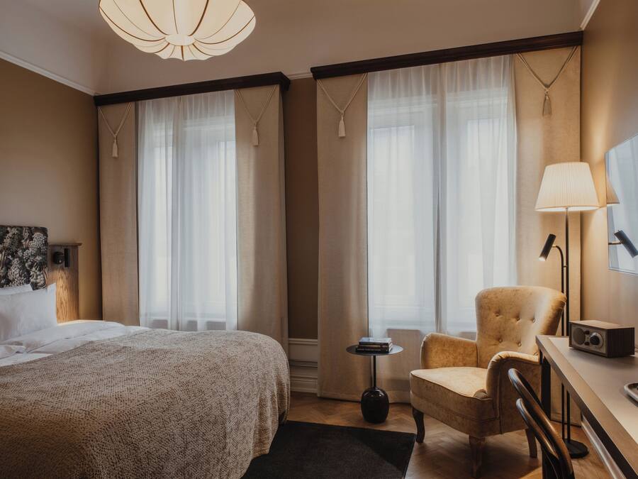 Ett hotellrum med en stor säng, en stol, ett skrivbord med en lampa och en tv.