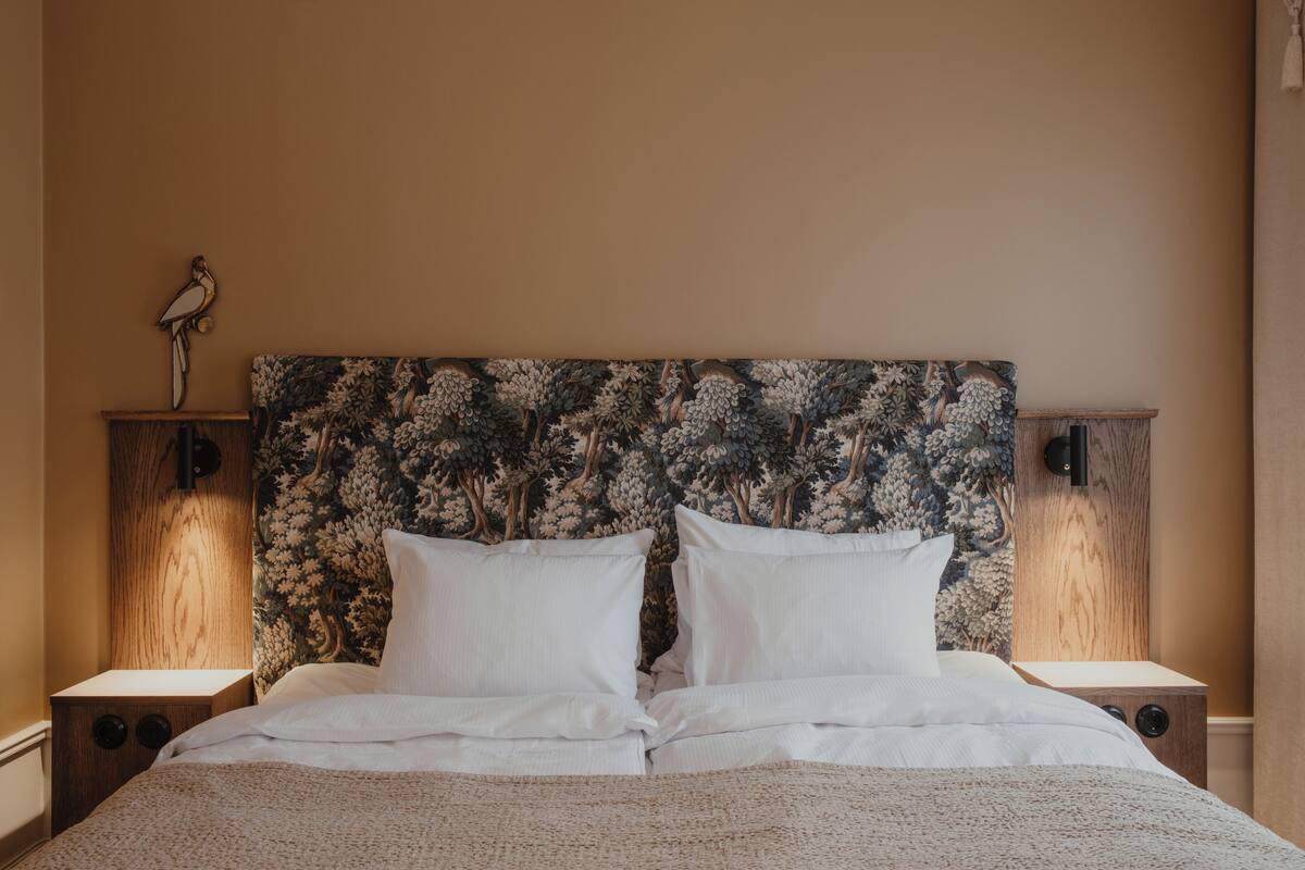 A neatly made bed with white linens, a floral-patterned headboard, and two bedside tables with lamps.
