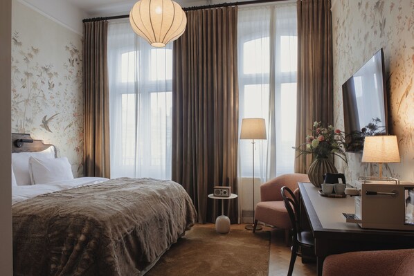 A hotel room with a bed, a desk with a lamp, a chair, and a TV on the wall. - Home Hotel Baltzar (Malmo)