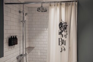 A bathroom with white tiled walls, a shower with a glass door, and a shower curtain with a black floral design. - Home Hotel Baltzar  (Malmo)