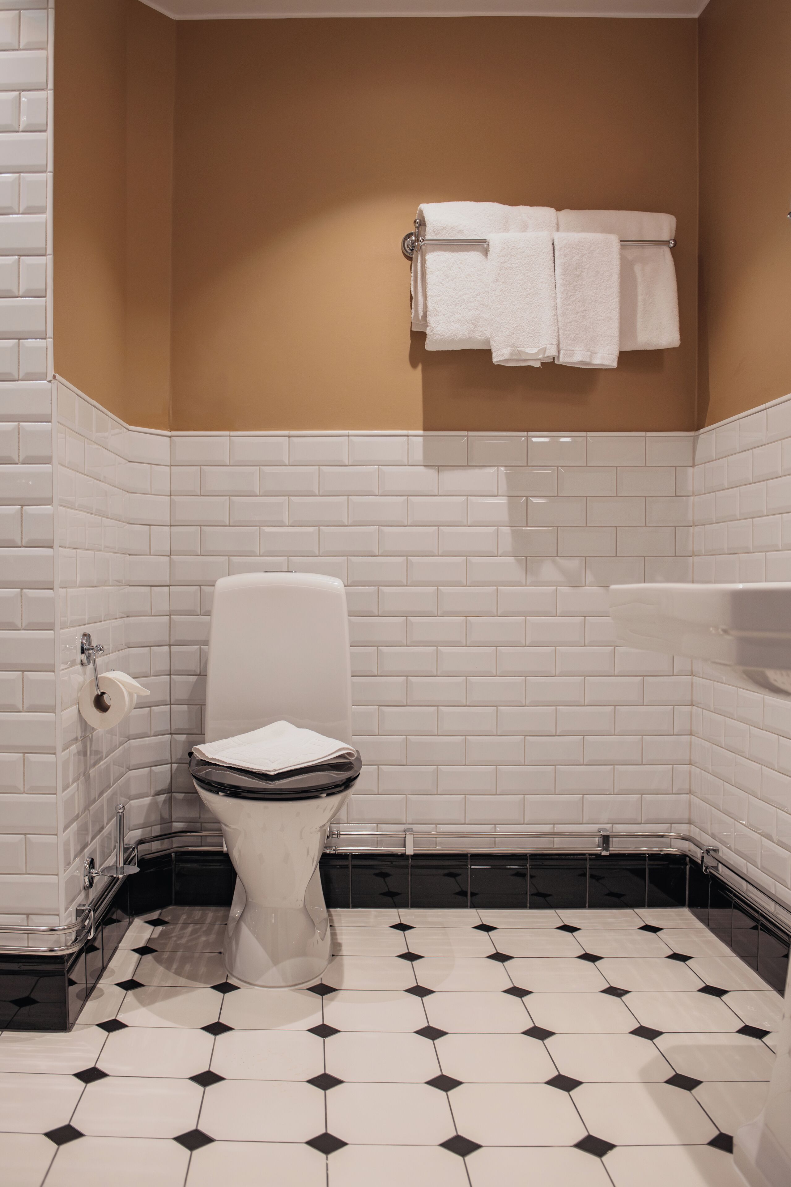 Un baño con azulejos blancos tipo metro, piso con estampado blanco y negro, y una pared de acento color beige.