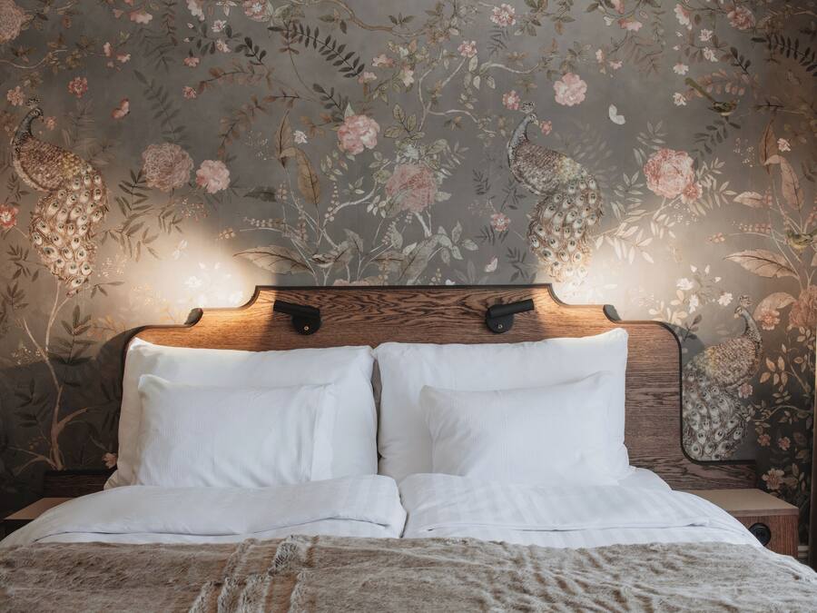 A bedroom with a floral wallpaper, a wooden headboard, and white bedding.