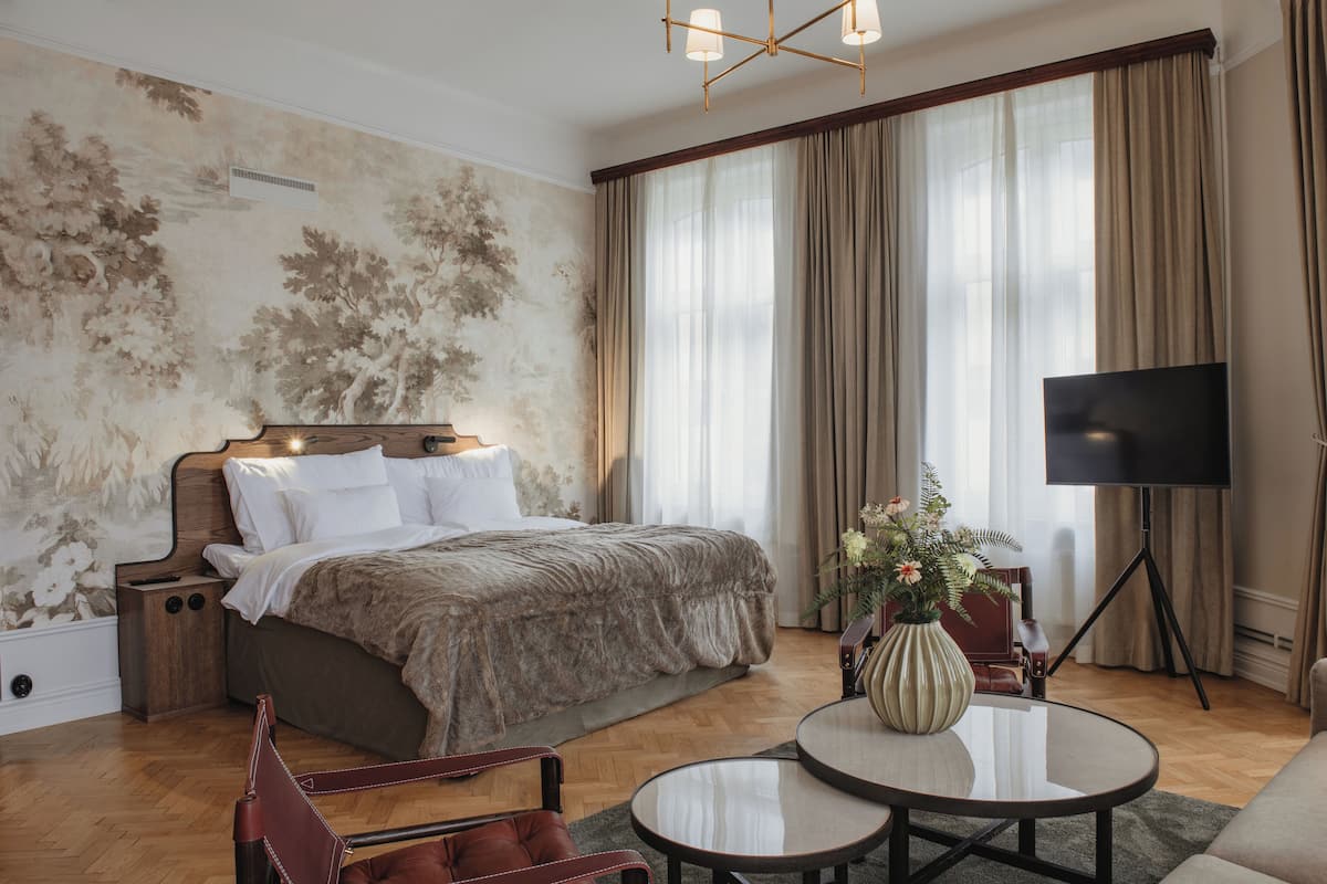 A bedroom with a large bed, a TV on a stand, a coffee table, and a chair.