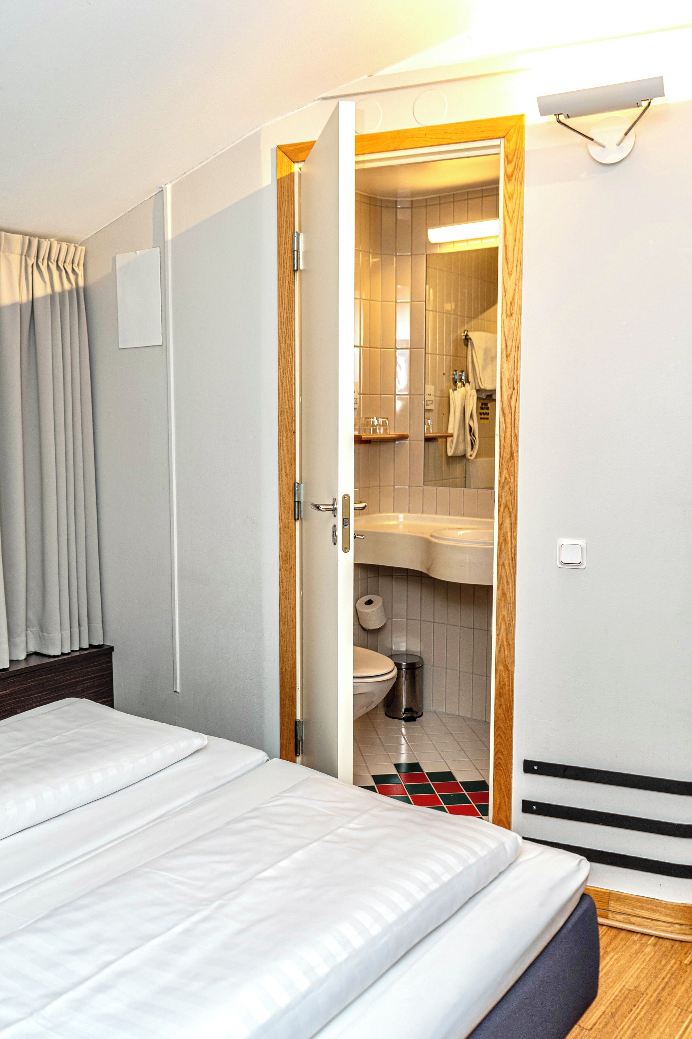 Una habitación de hotel con cama, baño con lavamanos e inodoro, y una puerta de madera.