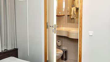 A hotel room with a bed, a bathroom with a sink and toilet, and a wooden door.