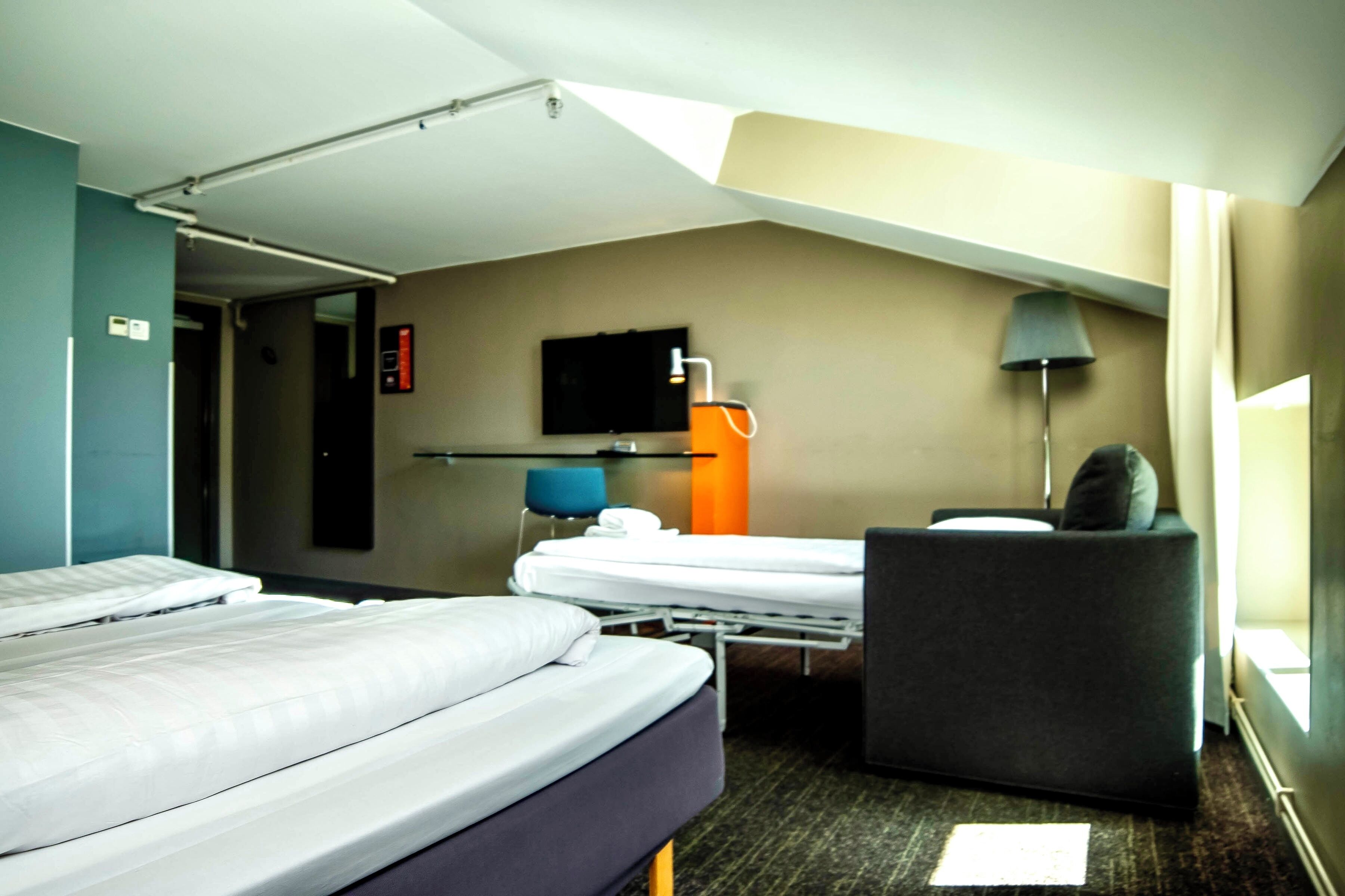 A hotel room with two beds, a desk, a chair, a TV, and a window.