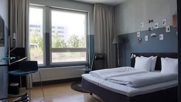 Habitación de hotel con cama, escritorio, silla y ventana con vistas a edificios y árboles.