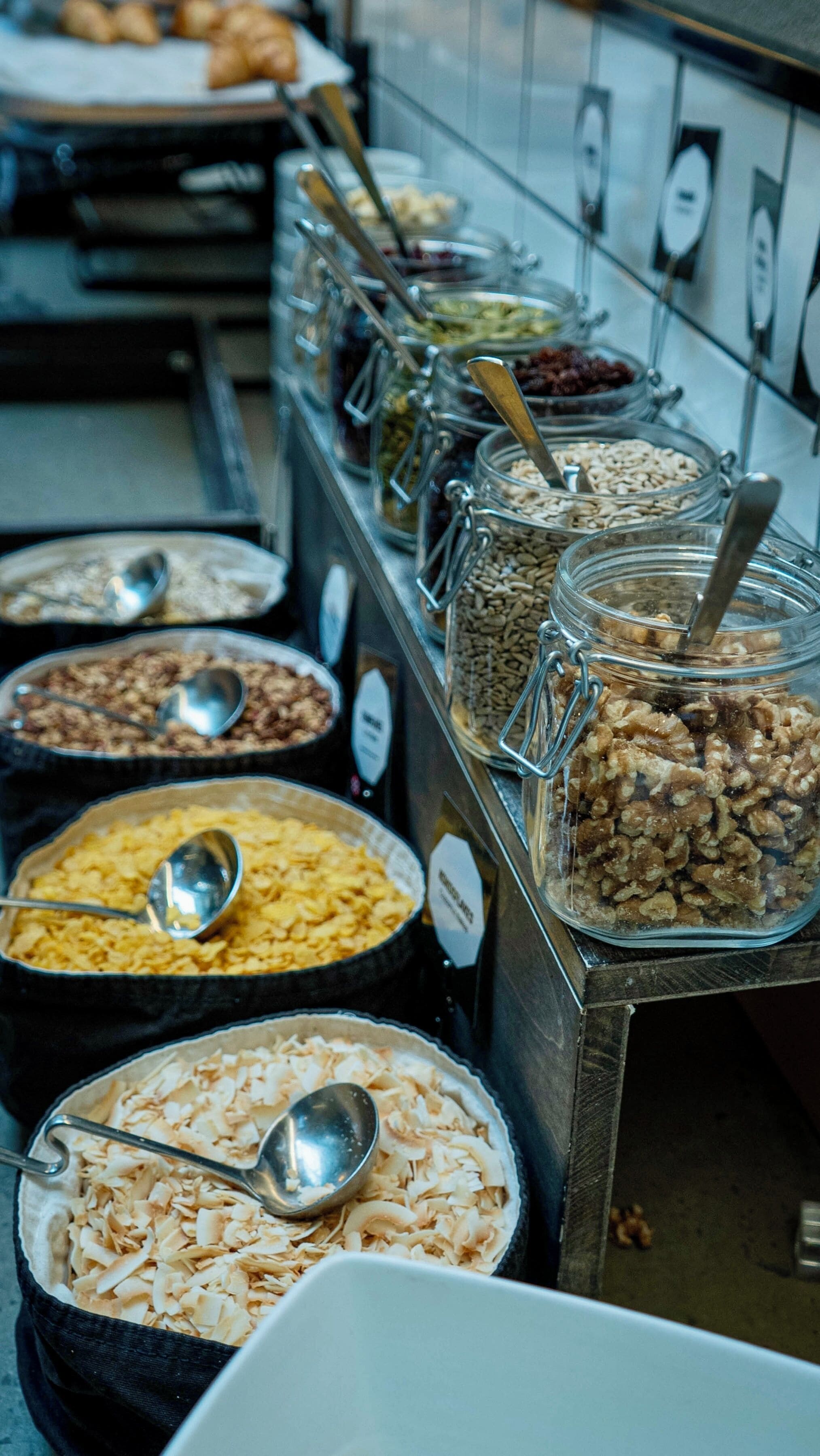 Un bufé con diversos alimentos en recipientes de vidrio, cada uno con una cuchara.