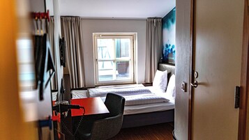 A hotel room with a bed, a desk, a chair, a television, and a window with curtains.