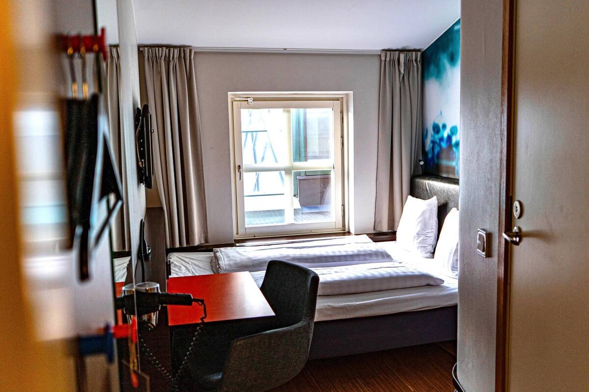 Una habitación de hotel con una cama, un escritorio, una silla y una ventana con cortinas.