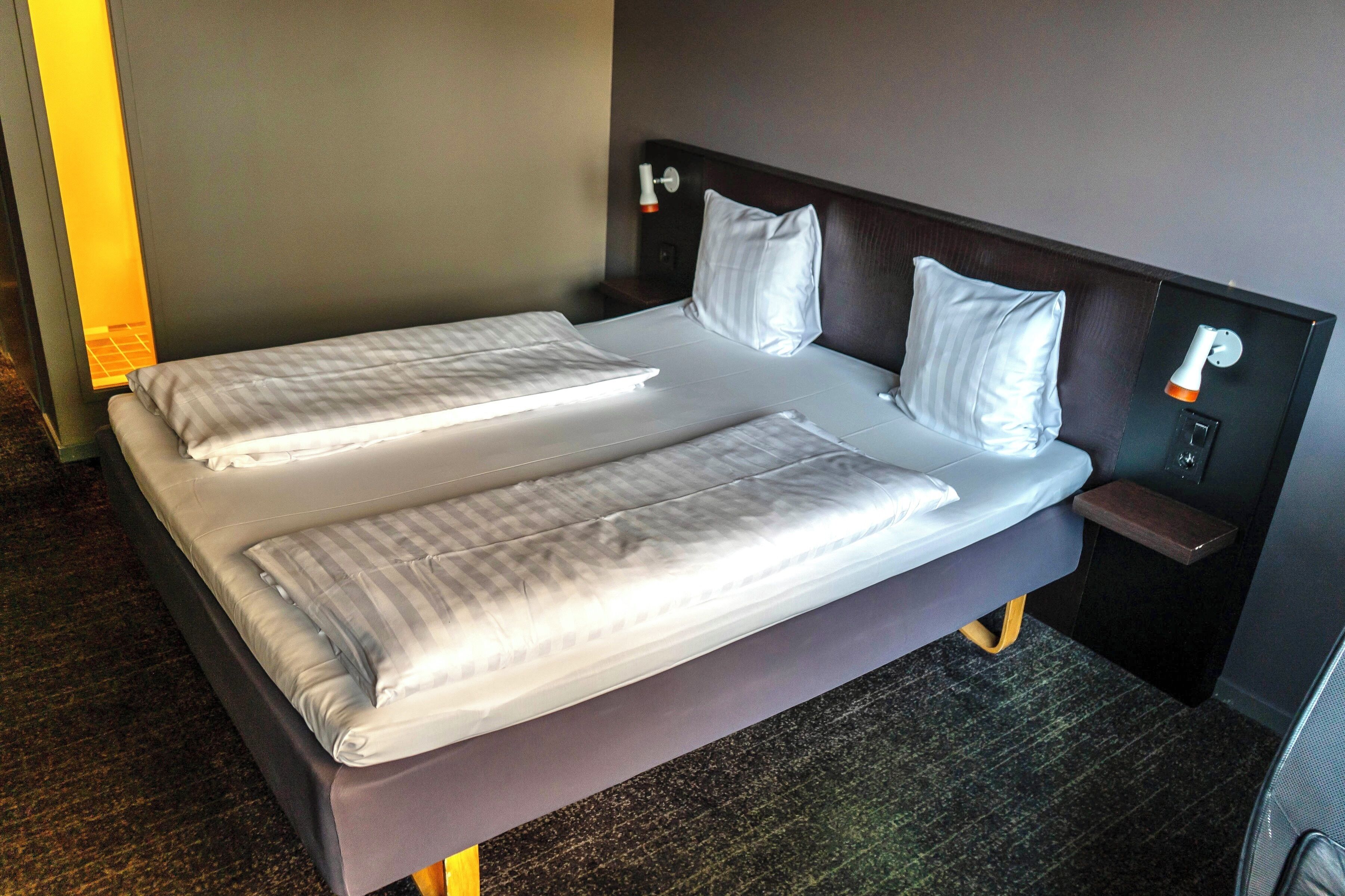 Una cama doble con dos almohadas, una mesita de noche y una lámpara de pared.