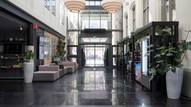 Een moderne hotel lobby met een glazen lift, zitgedeeltes en potplanten.