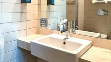 Een badkamer met een witte wasbak, zeepdispenser en een bordje dat vers en drinkbaar kraanwater aangeeft.