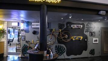 A self-check-in/out area with a neon sign, a bicycle, and a wall with plant and leaf designs.