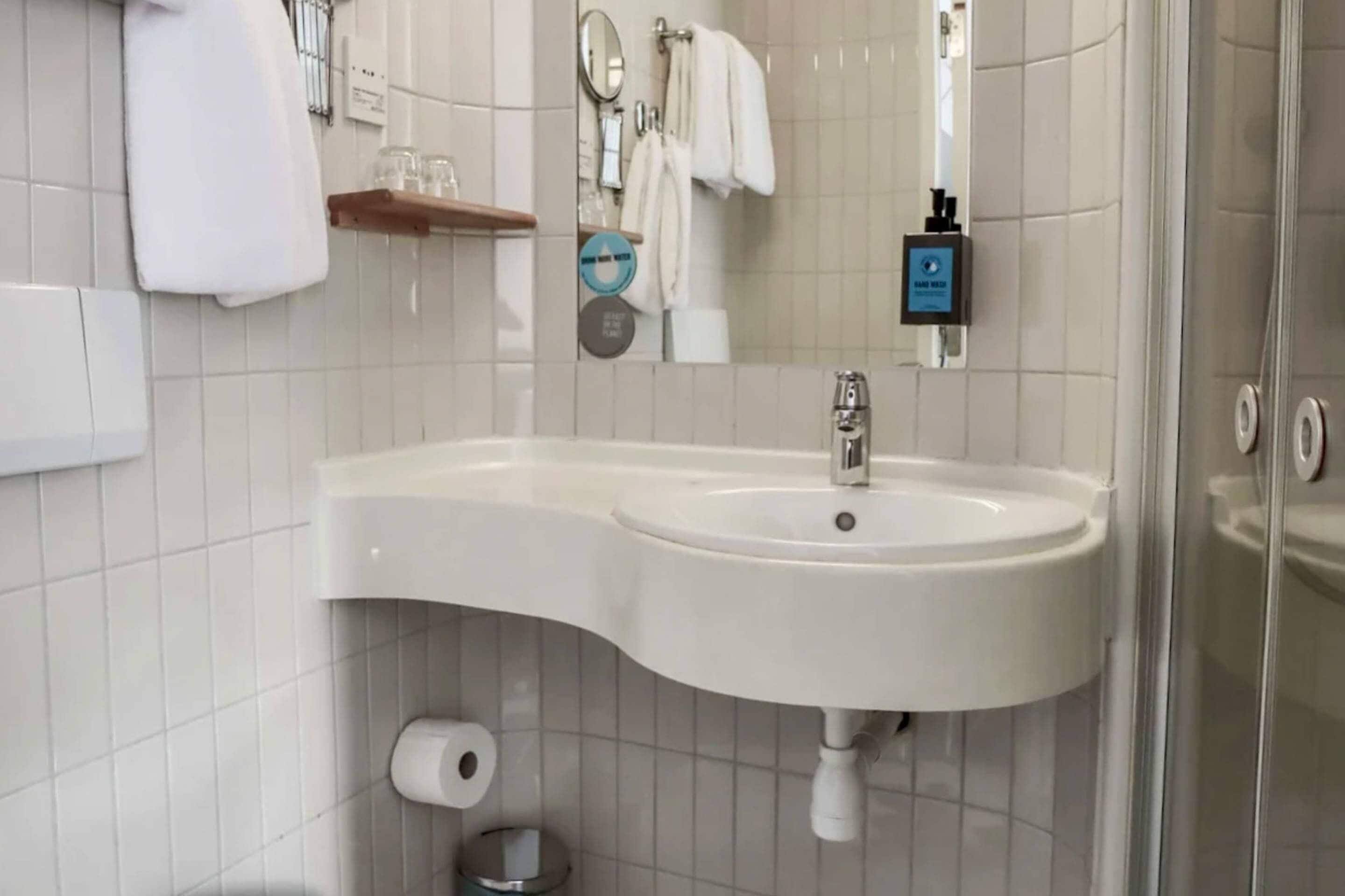 A bathroom with a white sink, a mirror, a towel rack, and a glass shower enclosure.