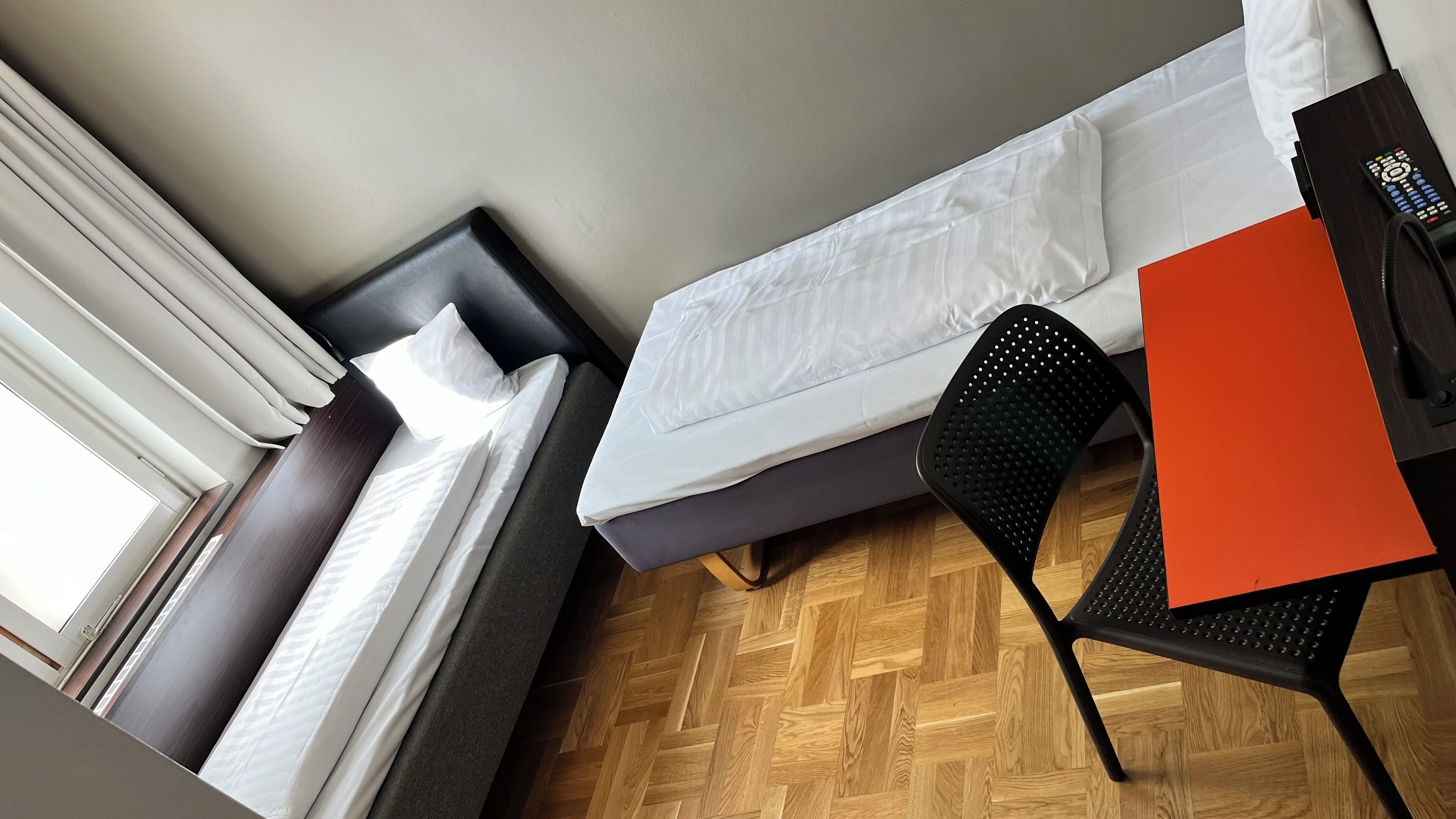 Een compacte hotelkamer met een enkel bed, een klein bureau, een stoel en een raam met gordijnen.
