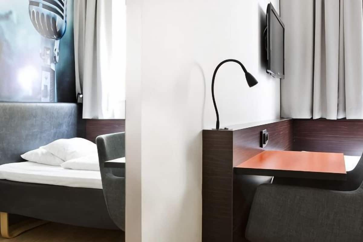Una habitación de hotel moderna con cama, escritorio con lámpara, televisor y ventana con cortinas.