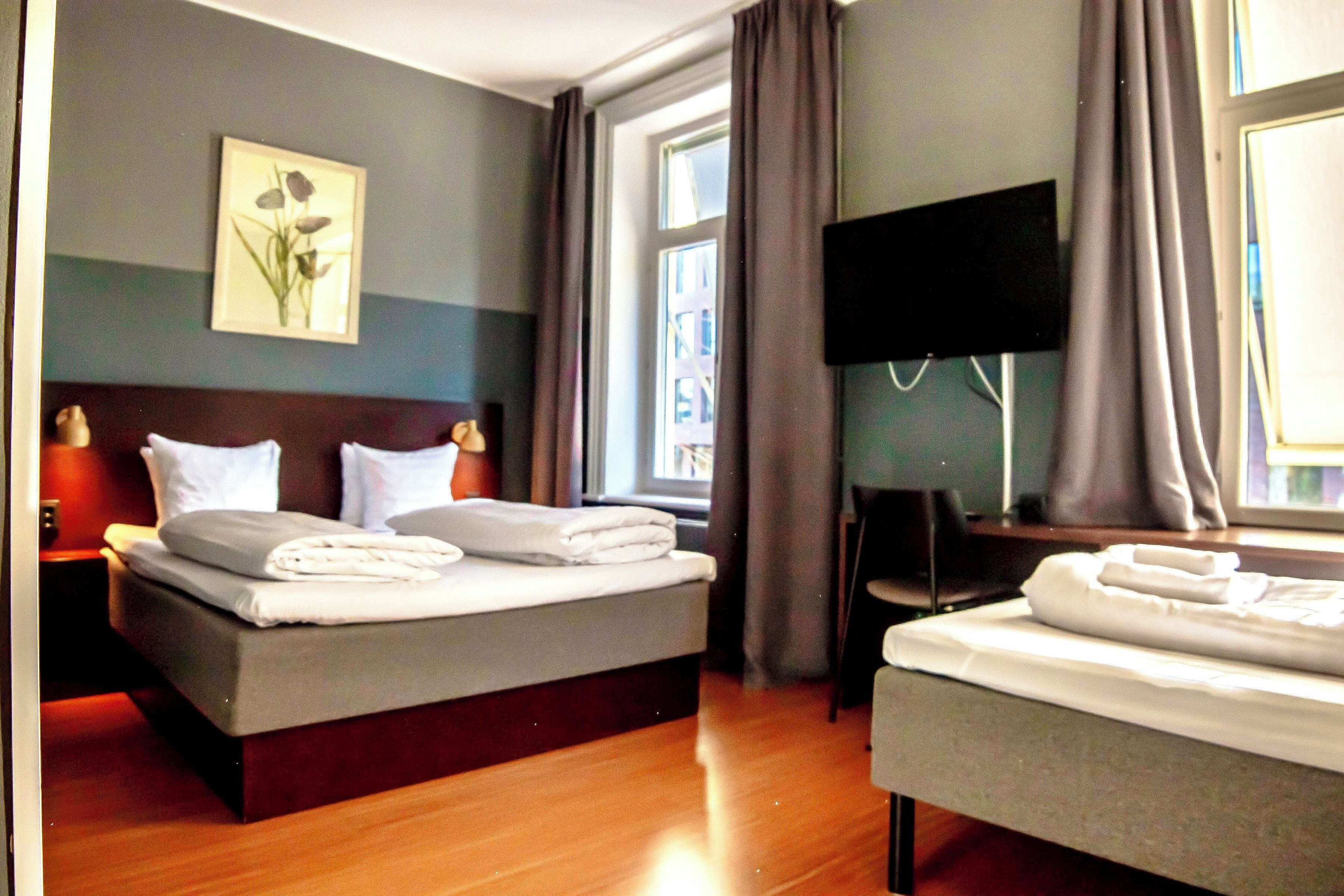 Una habitación de hotel con cama, mesita de noche, televisión y ventana con cortinas.