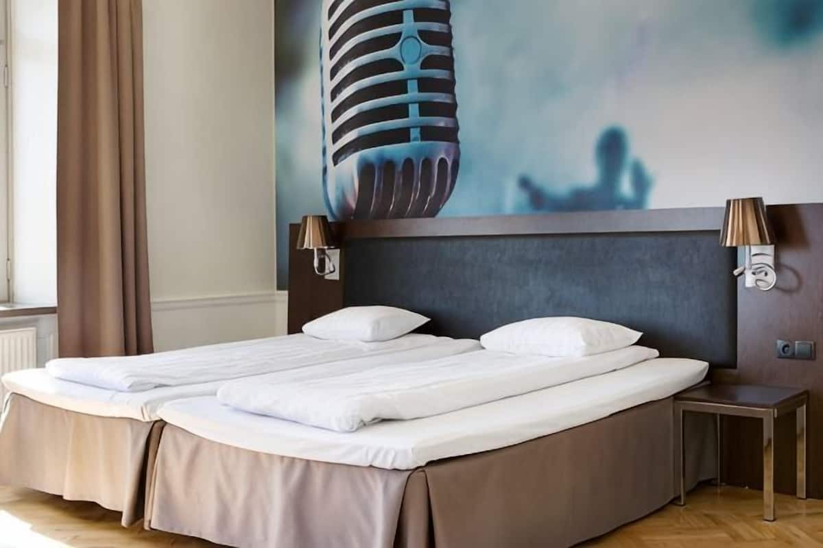Una cama doble con cabecera, dos mesitas de noche y una lámpara de pared.
