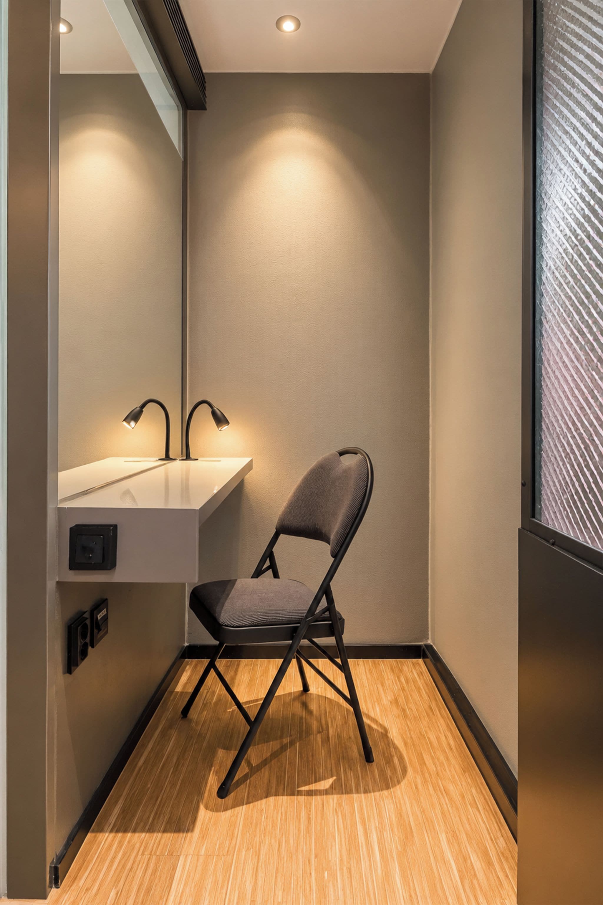 Ein modernes Badezimmer mit Holzboden, einem grauen Stuhl, einem weißen Waschbecken und einem Spiegel.