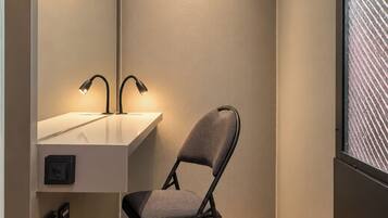 Ein modernes Badezimmer mit Holzboden, einem grauen Stuhl, einem weißen Waschbecken und einem Spiegel.