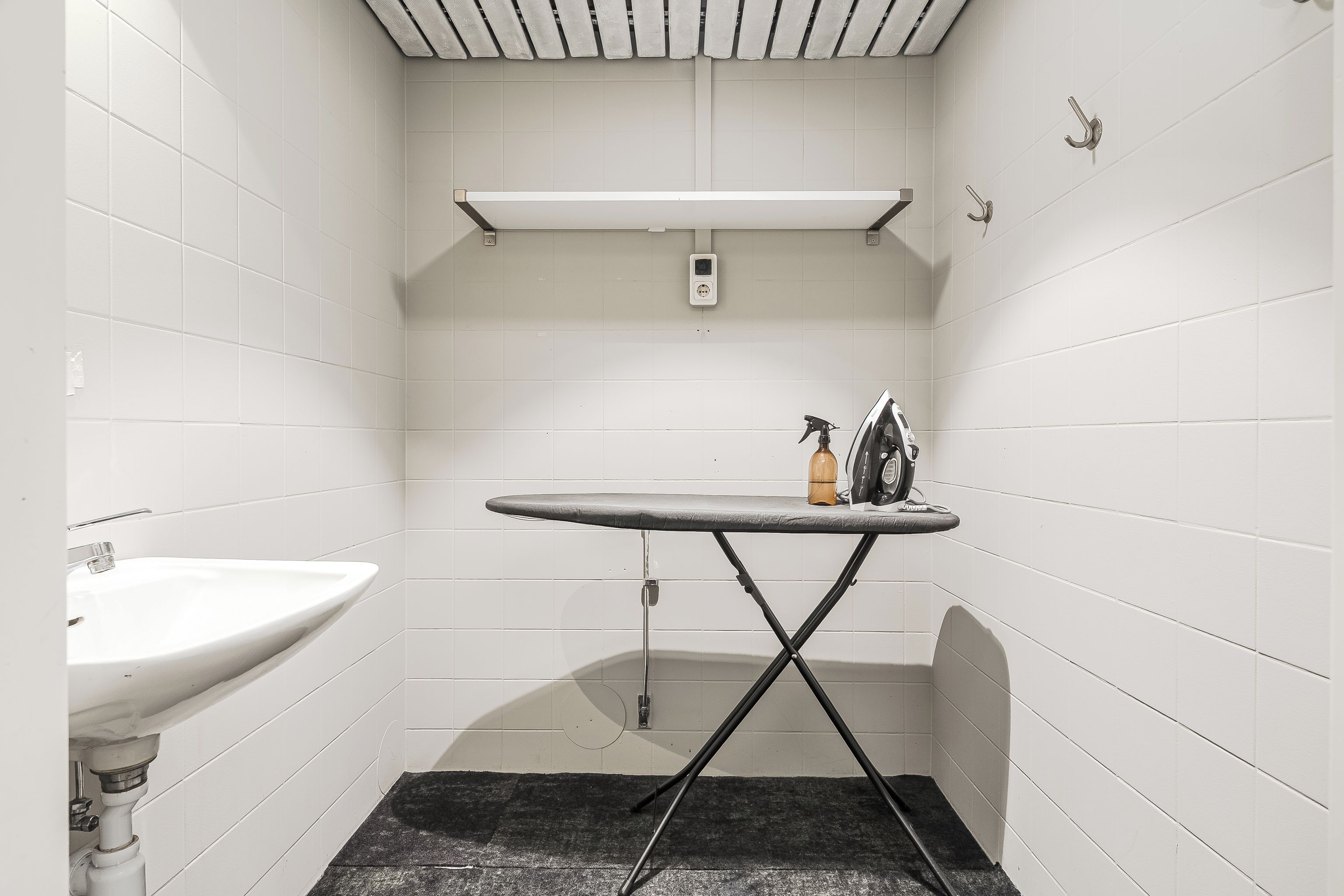 Un baño pequeño con paredes blancas, un lavabo, un perchero y un estante sobre el espejo.
