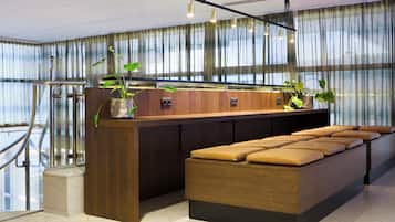 Un espace d’accueil moderne, doté d’un comptoir de réception en bois, de sièges confortables et de plantes en pot.