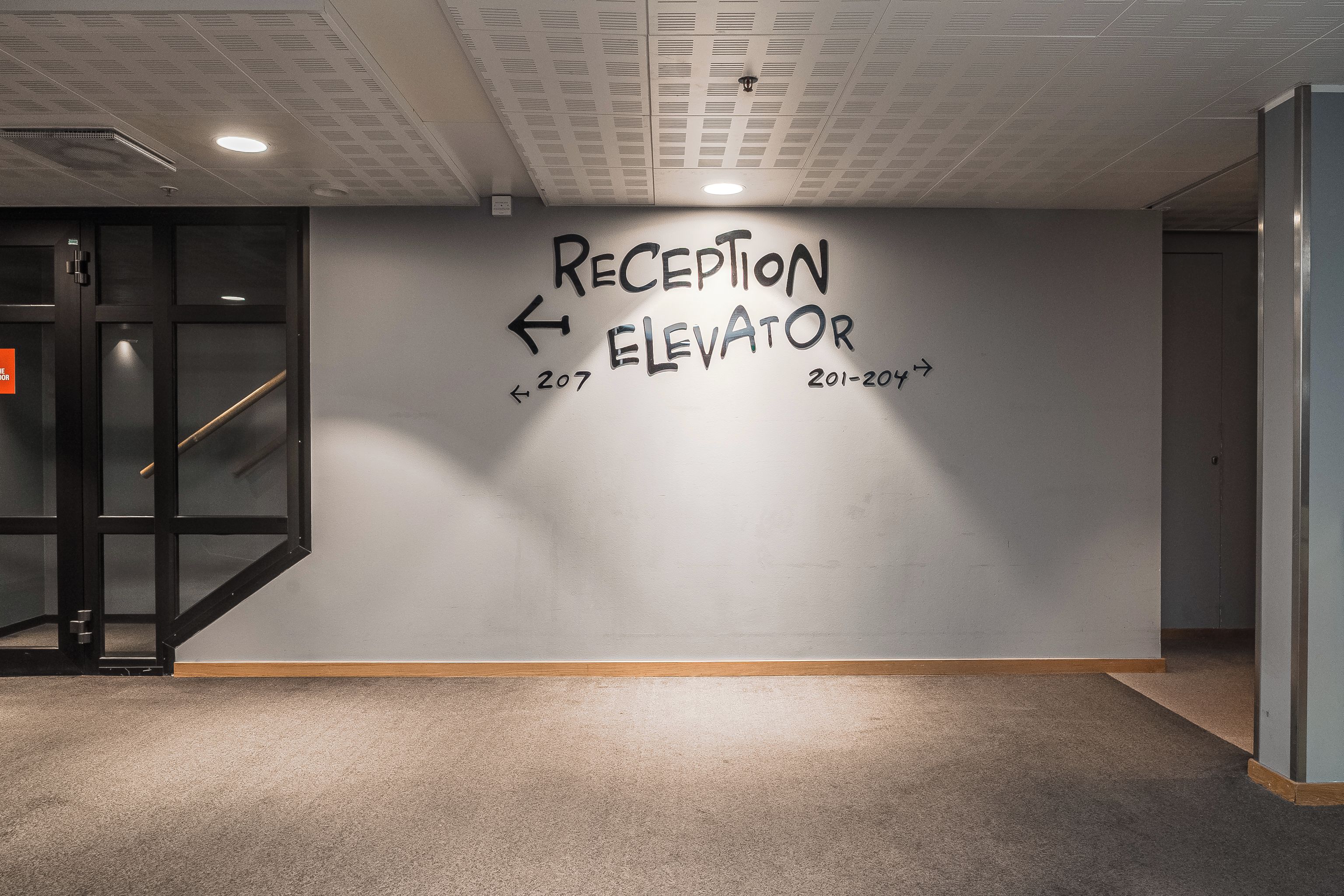 Ett receptionsområde med en väggskylt som visar var receptionen och hissen finns, samt att det är våning 207.