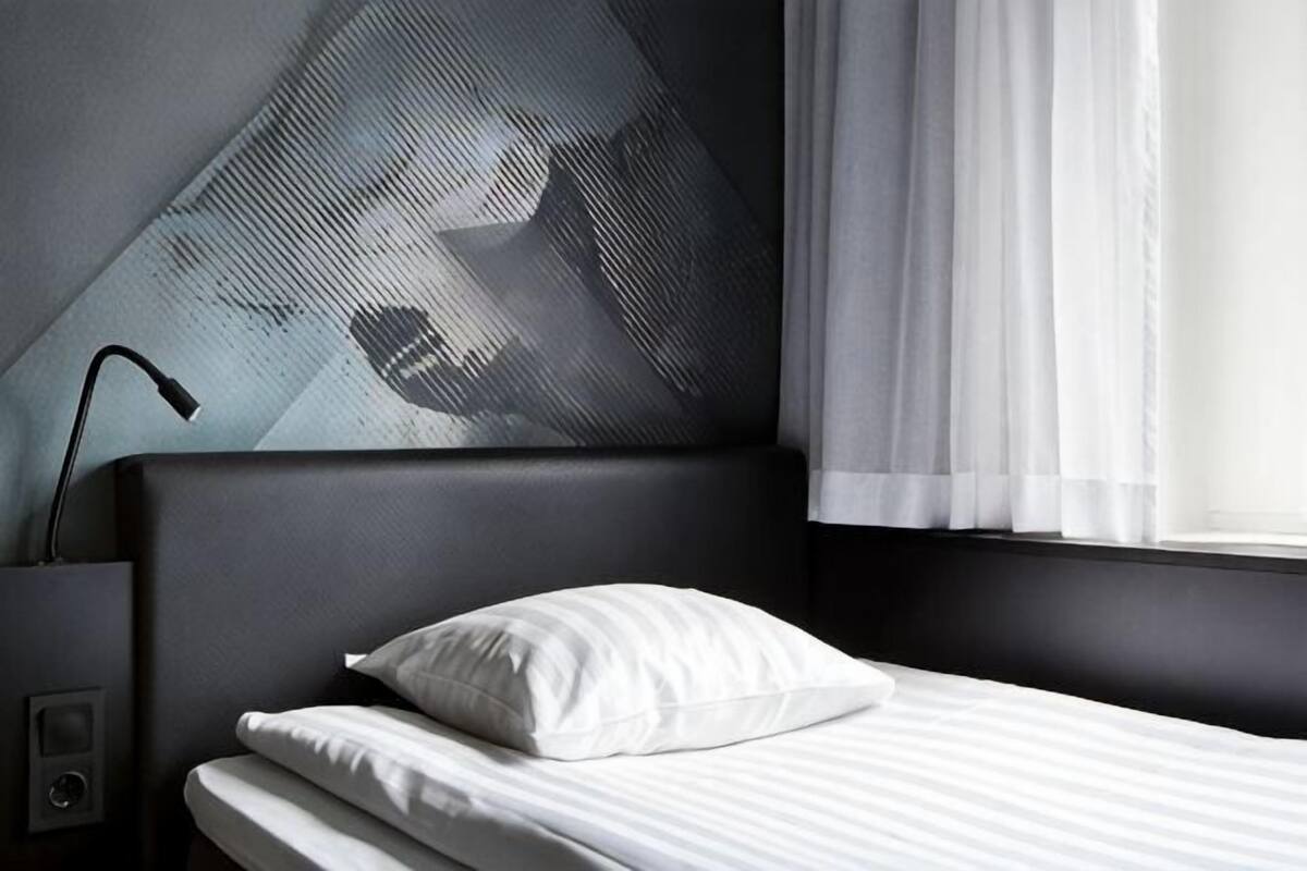 A hotel room with a bed, a nightstand, a lamp, and a wall with a geometric pattern.