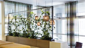 Ein moderner Empfangsbereich mit einem großen Fenster, einer Sitzecke mit Kissen und einem Pflanzenbeet mit Grünpflanzen.