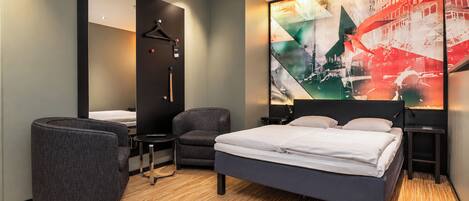 Una habitación de hotel moderna con una cama grande, dos sillones, un escritorio y un espejo.