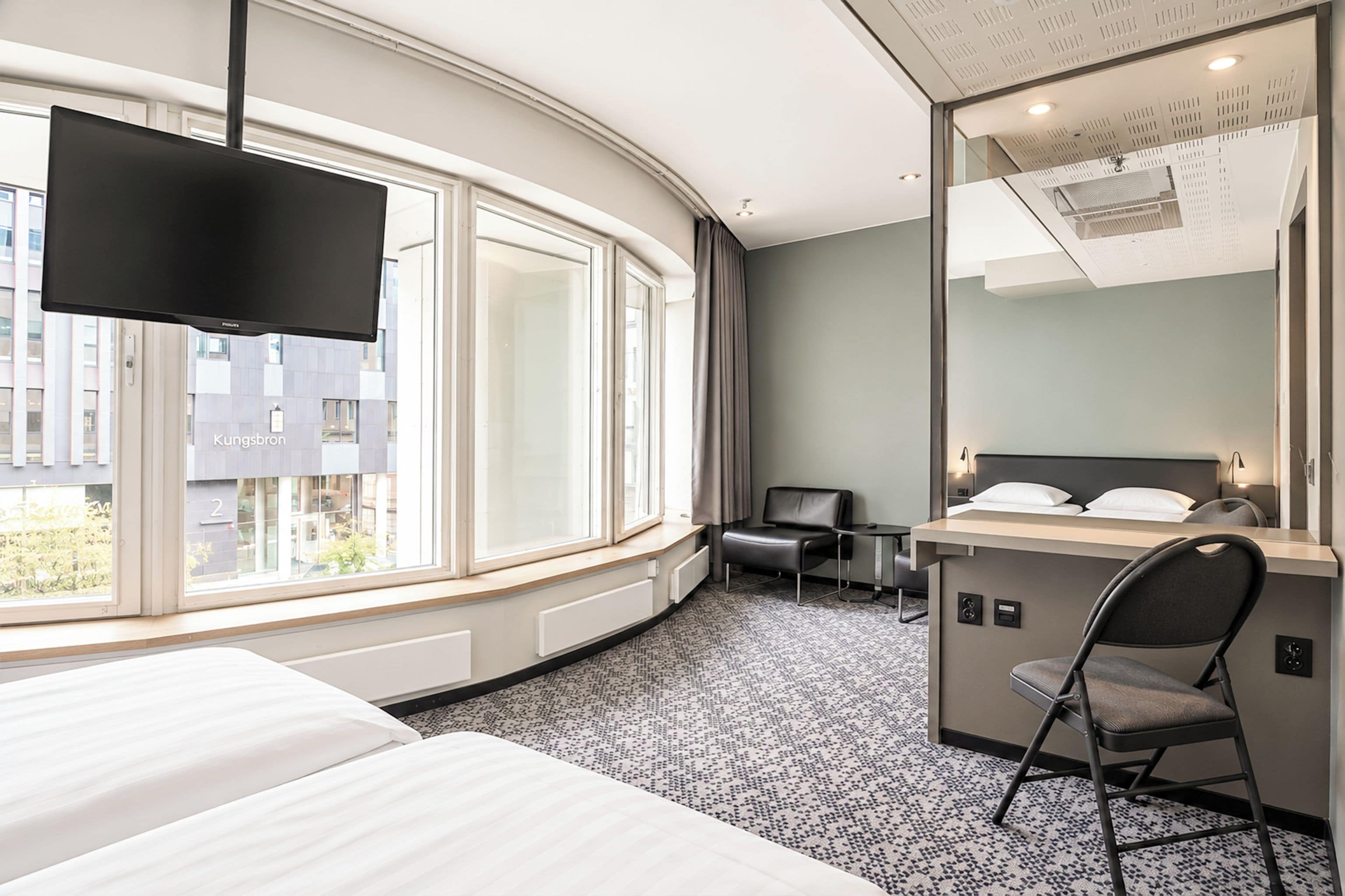 A hotel room with a bed, a desk, a chair, a television, and a large window.