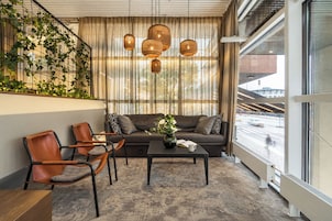 Una sala de estar moderna con un sofá, dos sillones, una mesa de centro y un amplio ventanal con cortinas.