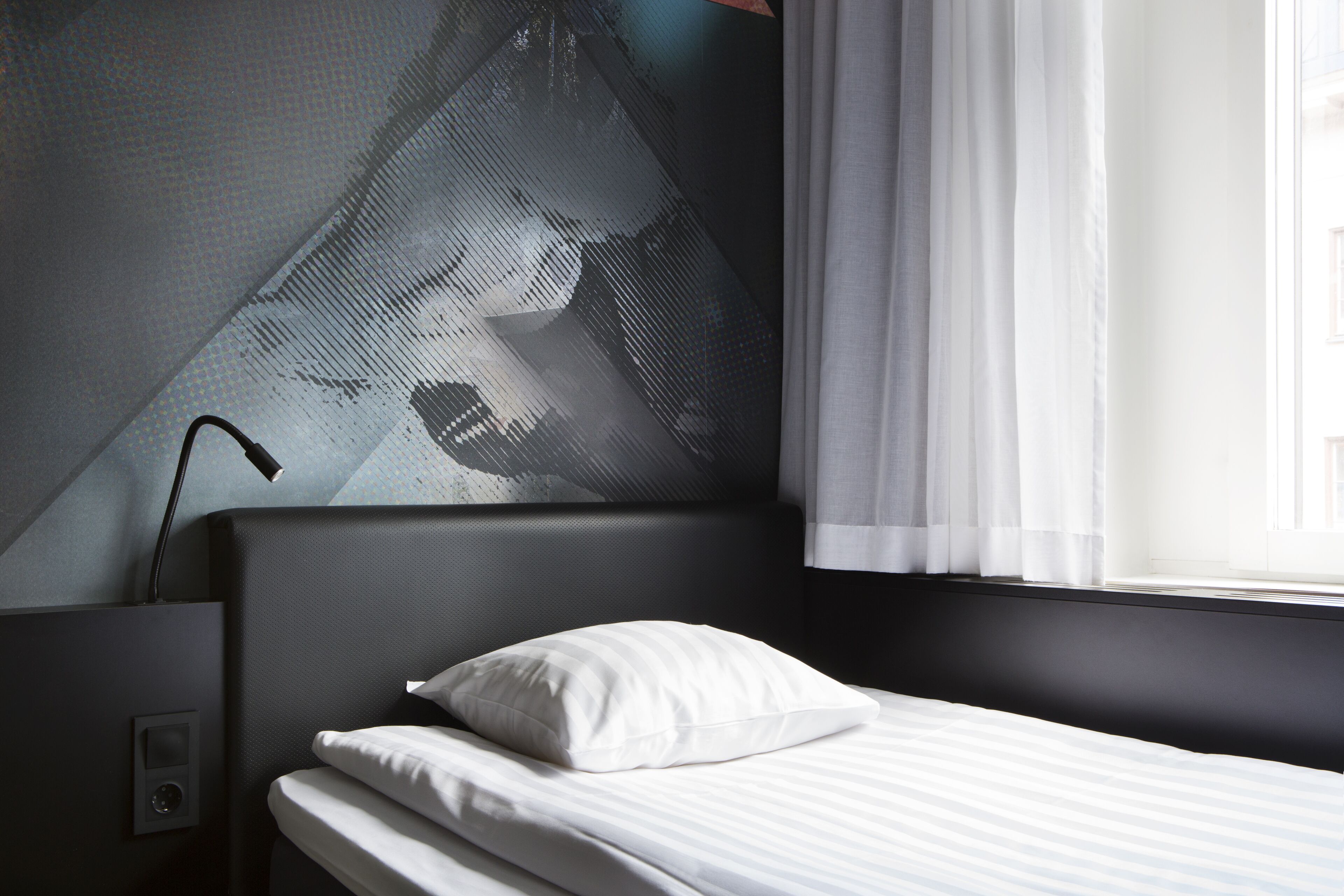Ein modernes Hotelzimmer mit großem Fenster, einem Bett mit weißer Bettwäsche und einer Wandlampe.