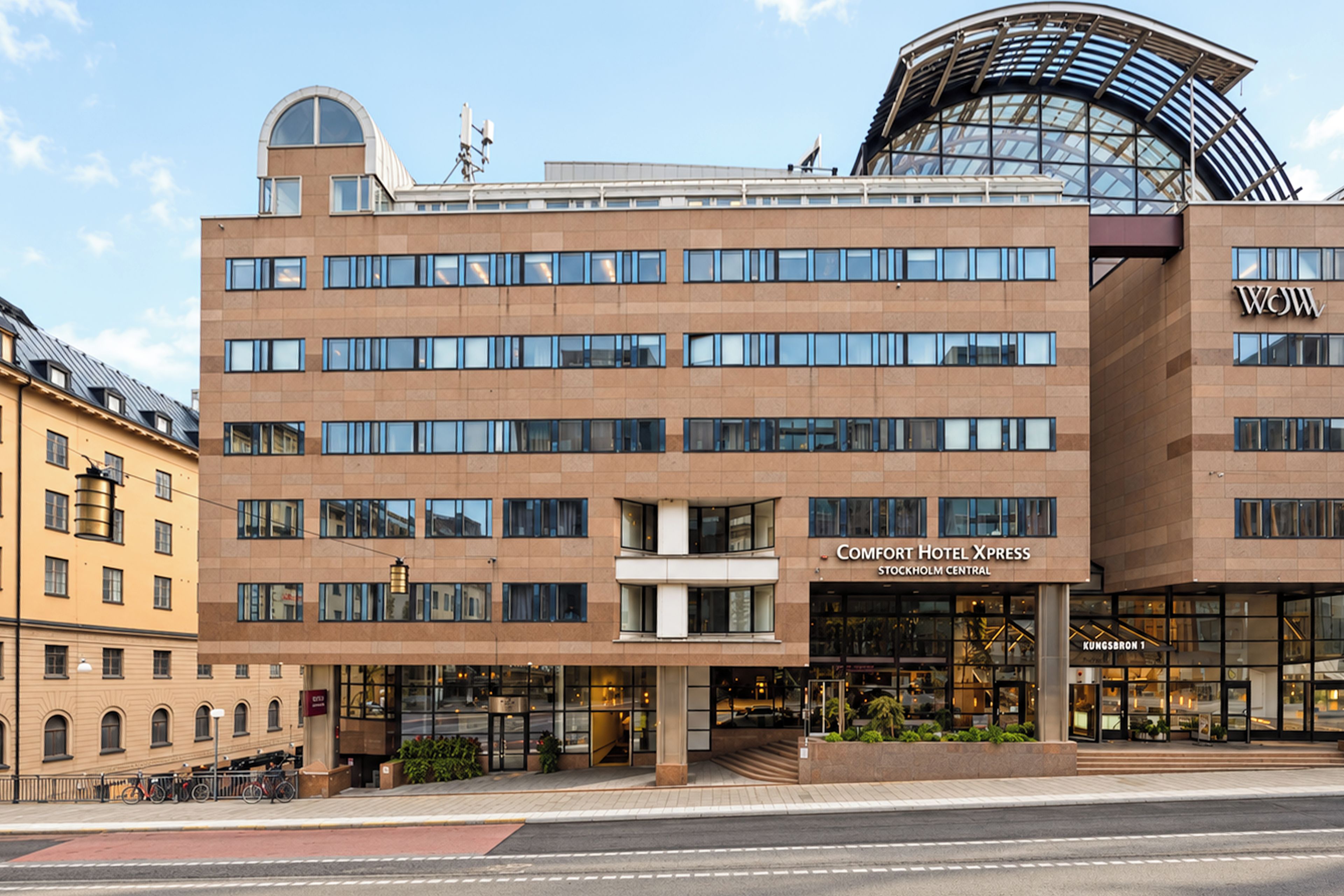 Een modern hotelgebouw met een opvallende ingang, meerdere verdiepingen en een opvallende, gebogen glazen constructie aan de rechterkant.