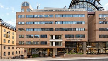 Een modern hotelgebouw met een opvallende ingang, meerdere verdiepingen en een opvallende, gebogen glazen constructie aan de rechterkant.