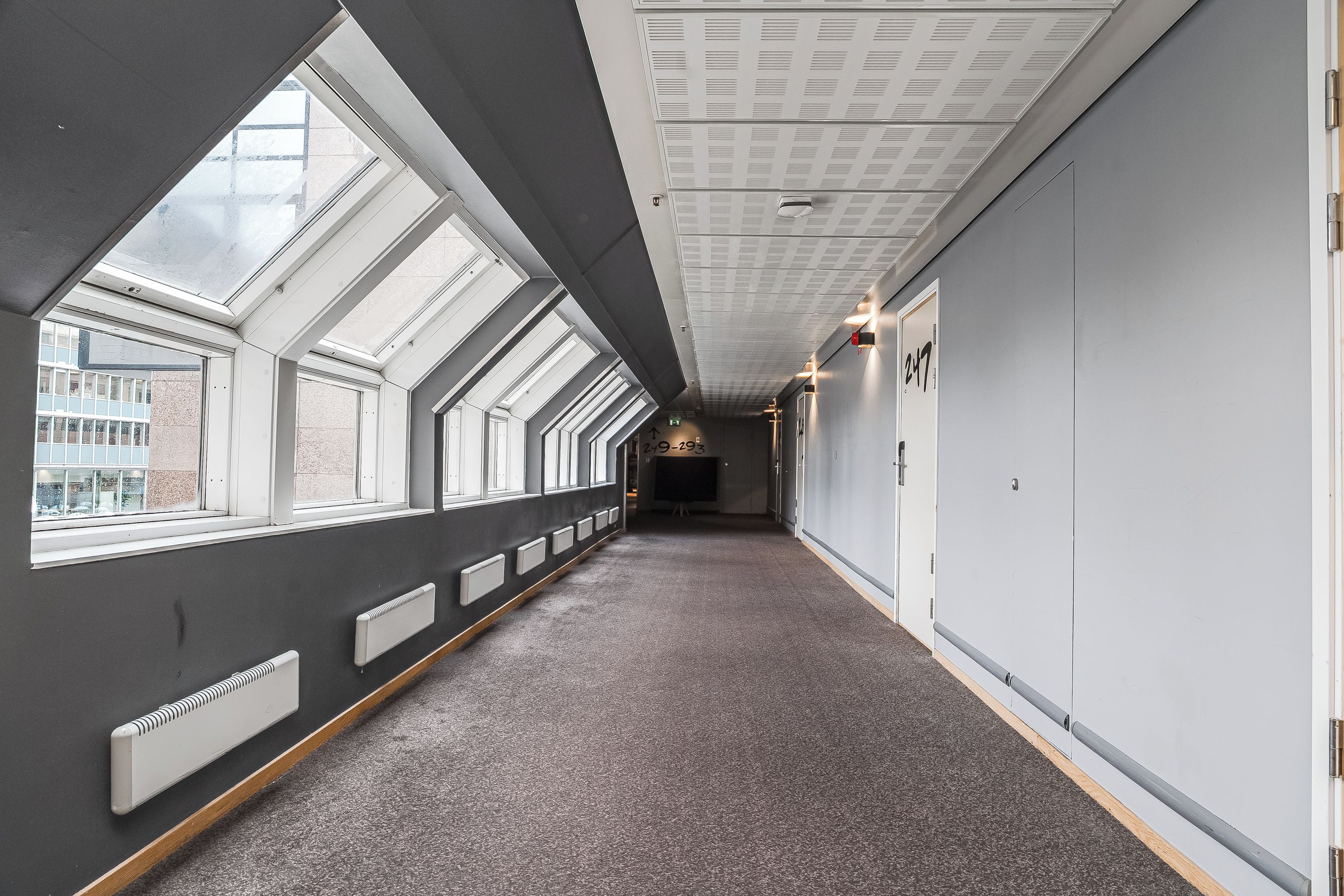 A corridor with skylights, a carpeted floor, and lockers on the right.