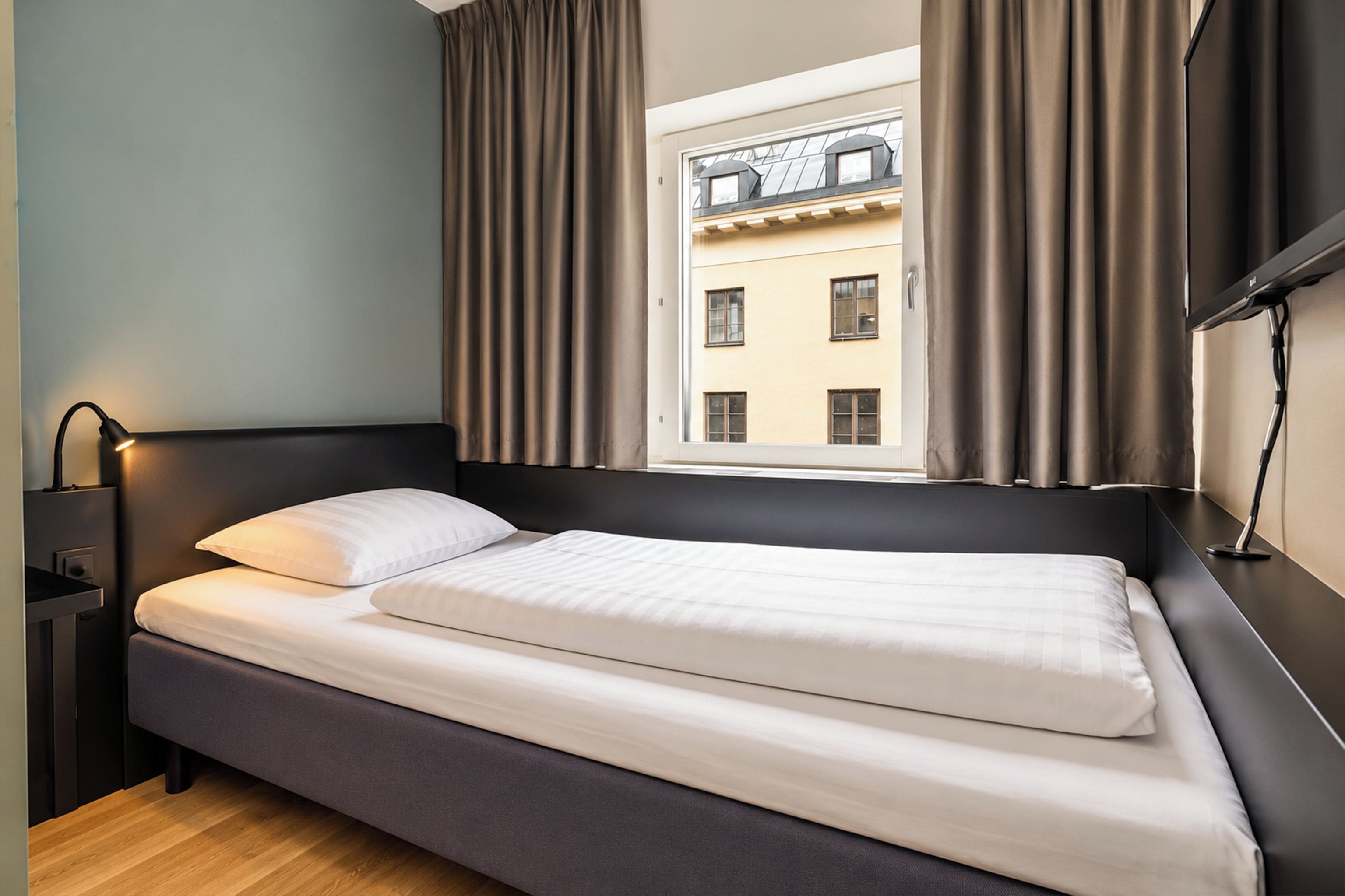 A single bed with a headboard, a bedside table with a lamp, and a window with curtains.