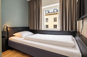 Una cama individual con cabecera, una mesita de noche con lámpara y una ventana con cortinas.