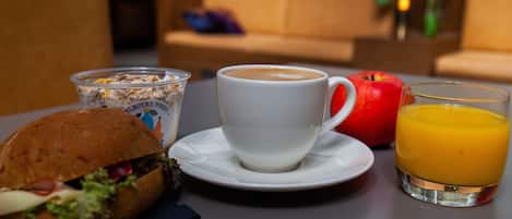 A breakfast setting with a sandwich, a cup of coffee, an apple, and a glass of orange juice on a table.