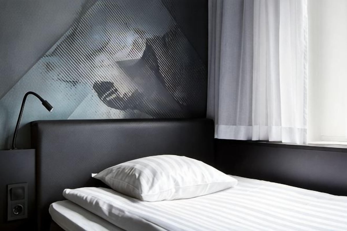 A hotel room with a bed, a nightstand, a lamp, and a wall with a geometric pattern.