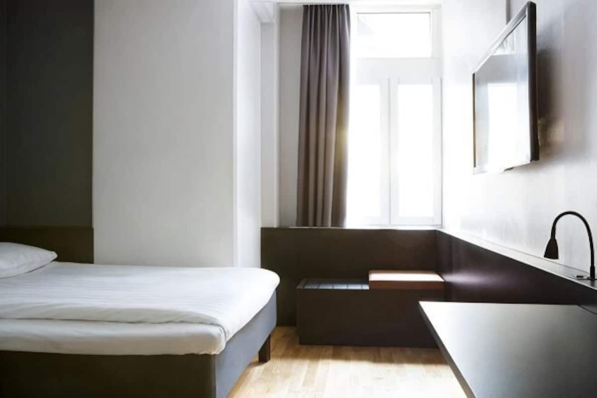 Une chambre dâhĂŽtel comprenant un lit, un petit coin salon, une fenĂȘtre avec des rideaux, un lavabo et un miroir.