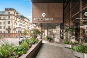 The entrance of Comfort Hotel Xpress with a modern facade, a clear sky, and a street view.
