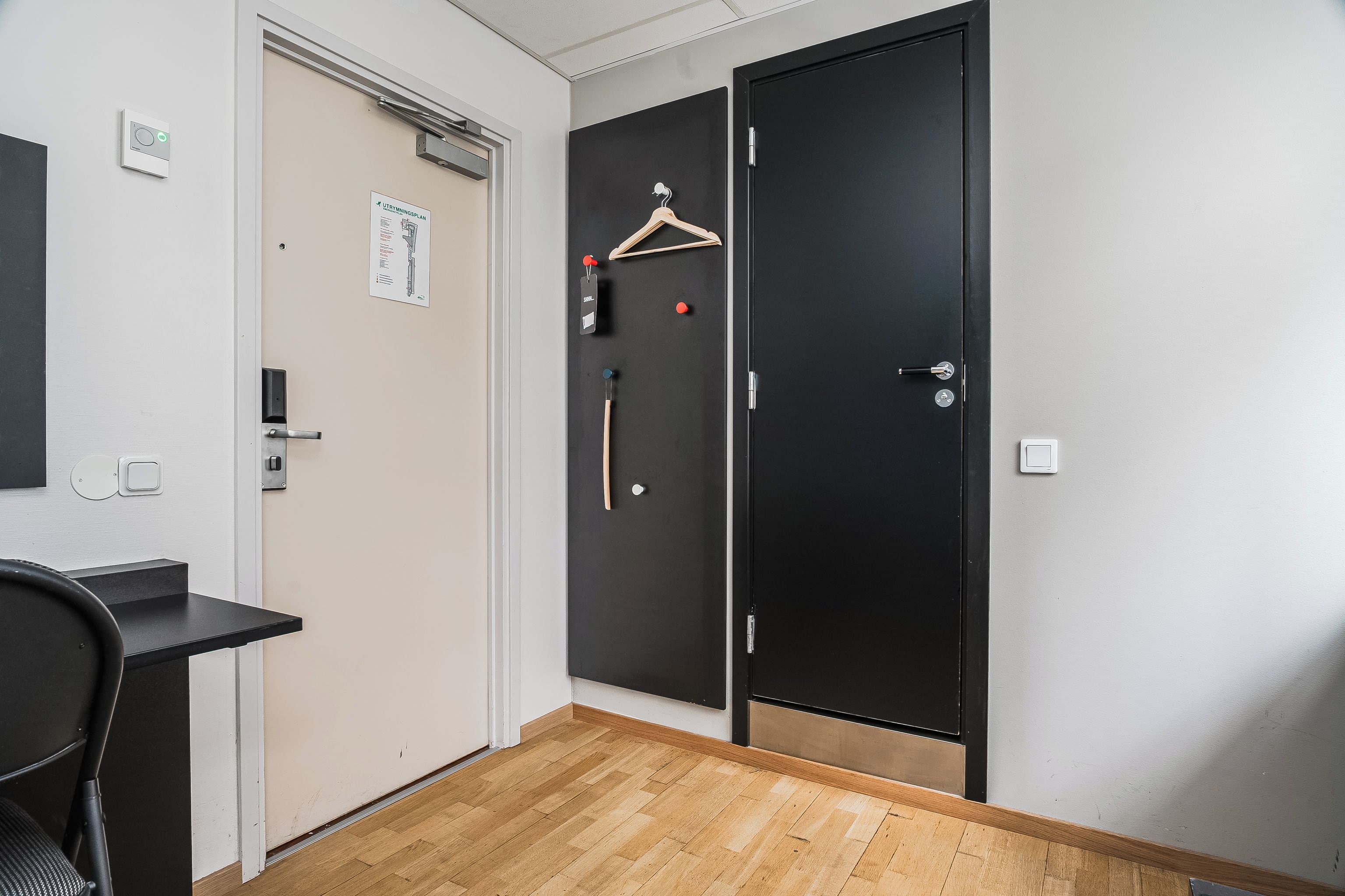 A hotel room with a desk, a black door, and a coat rack with hangers.