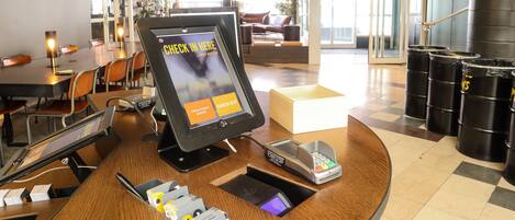 Un quiosco de registro en el vestíbulo de un hotel, con pantalla digital, zona de estar y una escalera.