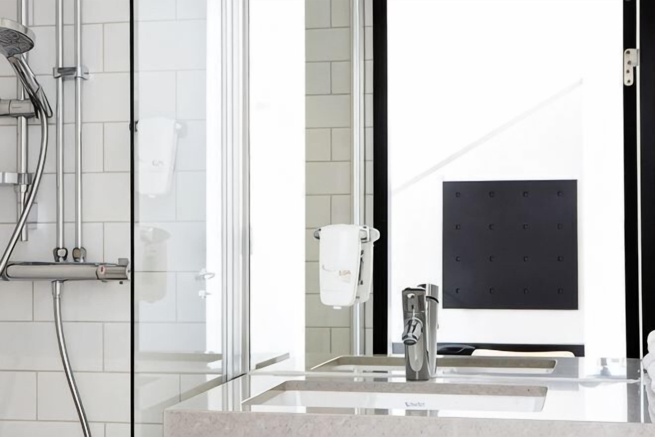 A modern bathroom with a glass shower enclosure, a sink with a mirror, and a towel rack.