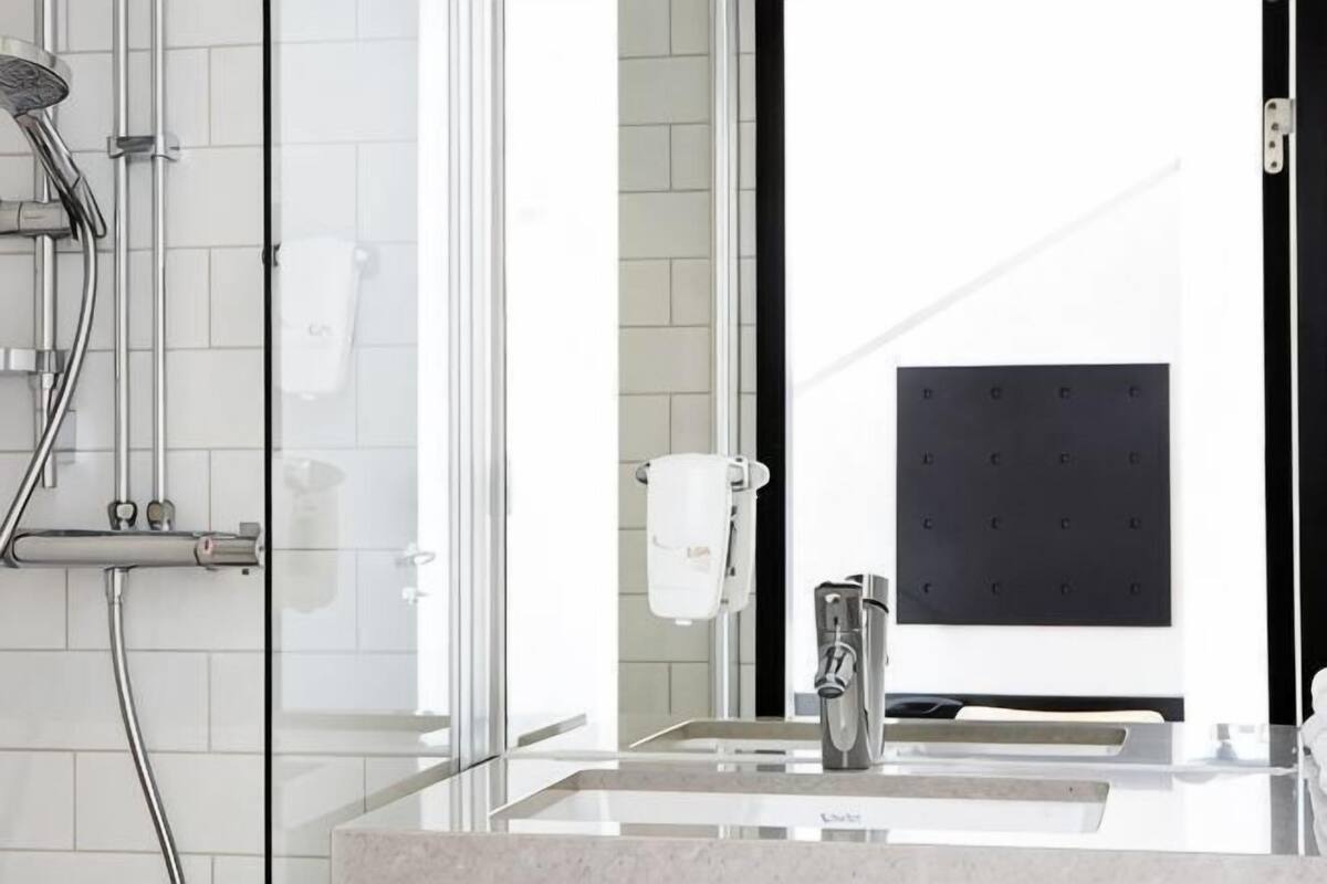 A modern bathroom with a glass shower enclosure, a sink with a mirror, and a towel dispenser.