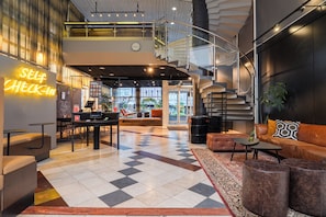 Een hotellobby met een receptiebalie, een zithoek en een trap.