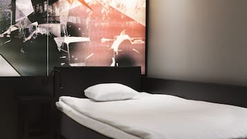 A modern hotel room with a single bed, a black nightstand, and a large mirror reflecting a cityscape.