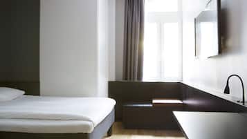 Une chambre d’hôtel moderne équipée d’un lit, d’une petite banquette, d’un lavabo et d’une fenêtre avec des rideaux.
